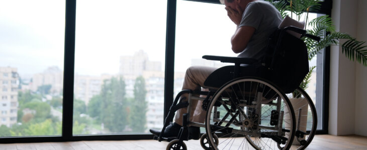 Elderly man in wheelchair crying near window indoors